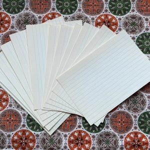 May include: A fan of lined index cards, fanned out on a patterned fabric. The cards are off-white with blue lines, and the fabric has a repeating pattern of circular designs in shades of brown, green, and gray.