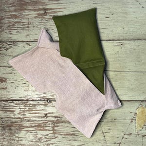 May include: A light pink and olive green eye mask. The light pink mask has a unique shape with a scalloped edge. The olive green mask is rectangular and fits inside the pink mask. The masks are made of fabric.