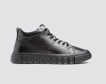 May include: Black high-top trainer with a thick, textured sole. The shoe features a leather upper, a lace-up closure, and a padded collar. The sole has a rectangular pattern. The trainer is designed for casual wear.