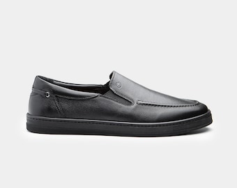May include: Black leather slip-on shoe with a rounded toe and a low-profile sole. The shoe features a stitched design on the vamp and a small decorative detail near the heel. The shoe is a solid black color.