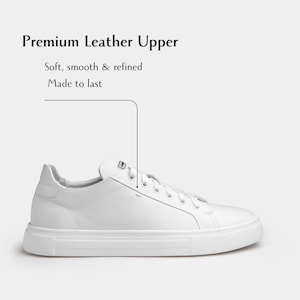 May include: A white leather sneaker with a thick sole. The shoe has a low-top design with white laces and a padded collar. The text "Premium Leather Upper" is displayed above the shoe, with the phrases "Soft, smooth & refined" and "Made to last" below it.