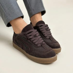 Può includere: Sneakers in camoscio marrone con dettagli in rete e lacci marroni. Le sneakers hanno una suola in gomma marrone. Le scarpe sono di stile casual.