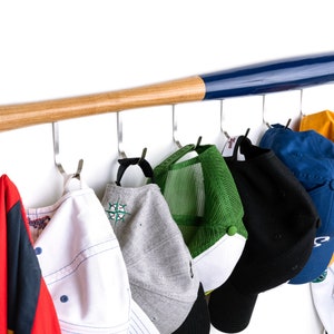 May include: A wooden baseball bat painted blue on one half, mounted on a wall with hooks.  The hooks hold a variety of hats, including baseball caps, a trucker hat, and a jacket.