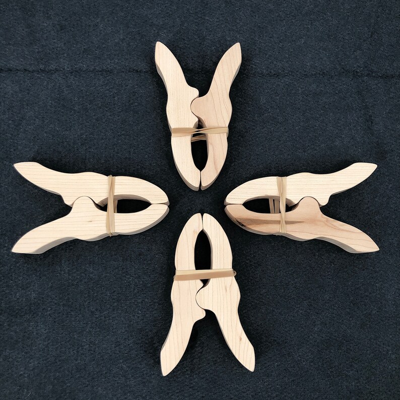 May include: Four wooden spring clamps with rubber bands. The clamps are arranged in a cross shape.