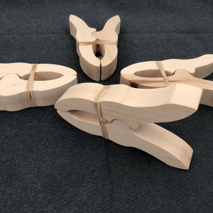 May include: Four wooden clothespins with rubber bands. The clothespins are made of natural wood and have a simple design.