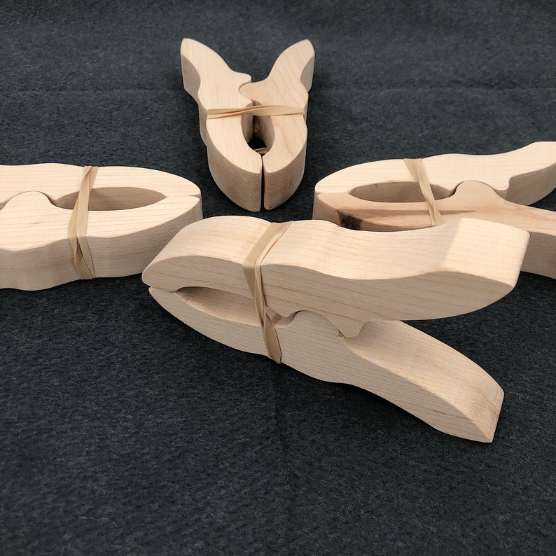 May include: Four wooden clothespins with rubber bands. The clothespins are made of natural wood and have a simple design.