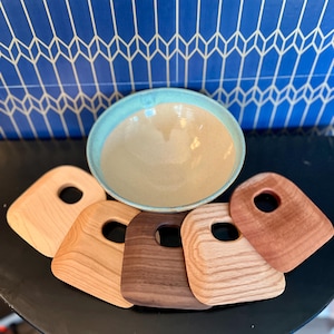 May include: Five wooden serving pieces with a hole in the centre, arranged around a light blue ceramic bowl. The serving pieces are made of different types of wood, including cherry, maple, and walnut.