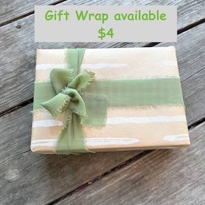 May include: A brown gift box with a green ribbon tied in a bow. The box has a white and brown striped pattern. The text "Gift Wrap available $4" is visible above the box.
