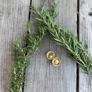 Pu&ograve; includere: Due tappi di bottiglia in metallo color oro su una superficie di legno con due rametti di rosmarino.