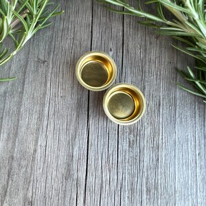 Pu&ograve; includere: Due piccoli portacandele rotondi in metallo dorato su una superficie di legno invecchiato.
