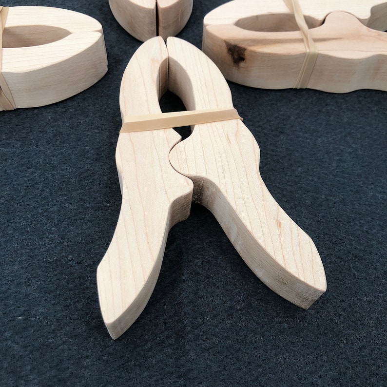May include: Two wooden spring clamps are joined together with a rubber band. The clamps are made of light wood and have a natural finish.