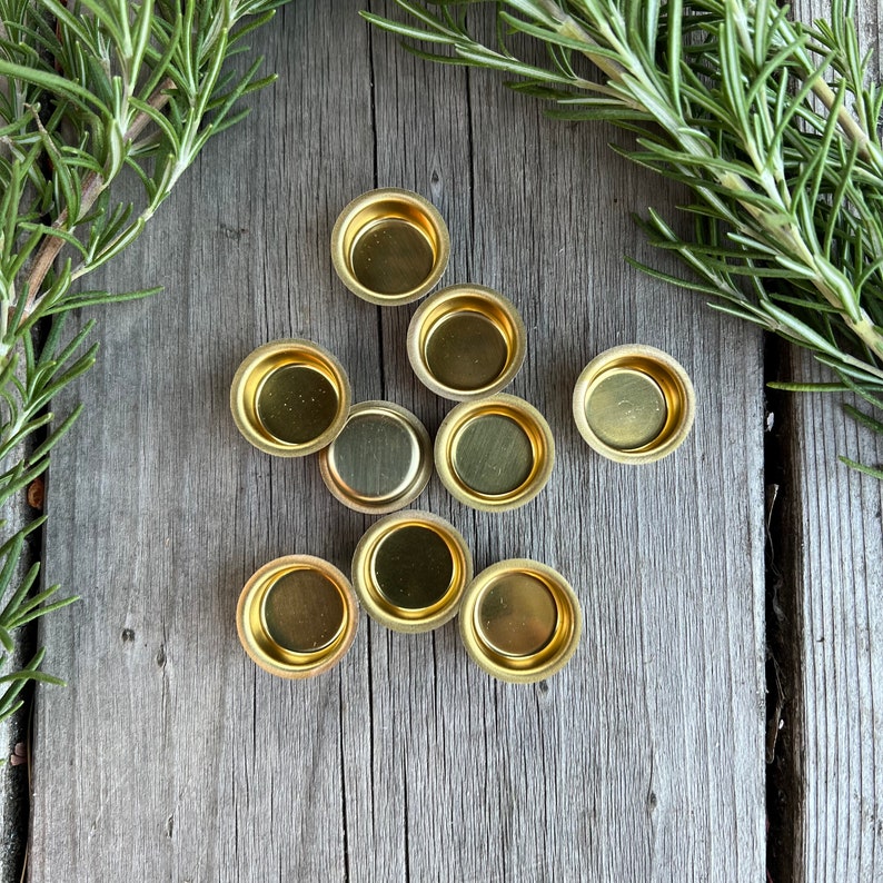 Pu&ograve; includere: Nove portacandele in metallo color oro su una superficie in legno. I portacandele sono rotondi e hanno un bordo leggermente rialzato.