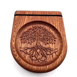 May include: A wooden box with a carved tree of life design. The box is made of a reddish-brown wood and has a curved shape. The tree design is in the center of the box and is intricately carved with detailed leaves and roots.