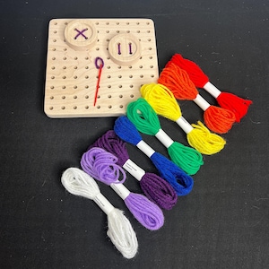 May include: A wooden pegboard with two buttons and a needle, along with eight spools of colorful yarn in rainbow order: red, orange, yellow, green, blue, purple, lavender, and white.