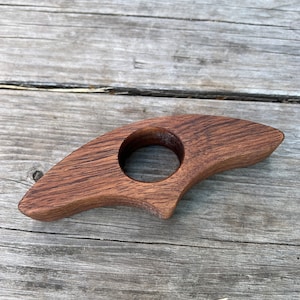 May include: A wooden ring holder shaped like a crescent moon with a smooth, dark brown finish.