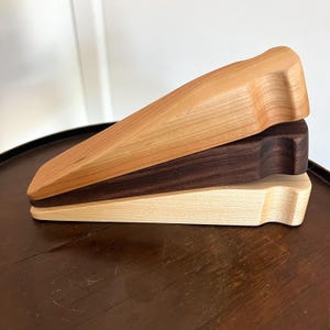 May include: Three wooden bottle stoppers in different wood types: cherry, walnut, and maple. The stoppers are stacked on top of each other.
