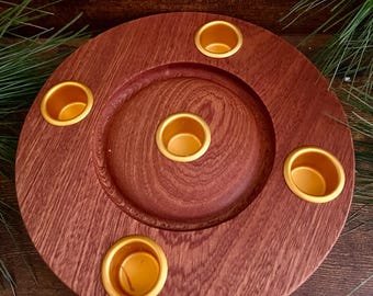 May include: A round, wooden candle holder with a rich, reddish-brown finish. It features five gold-colored candle cups arranged in a circular pattern. The holder is designed to hold multiple candles, creating a warm and inviting ambiance.