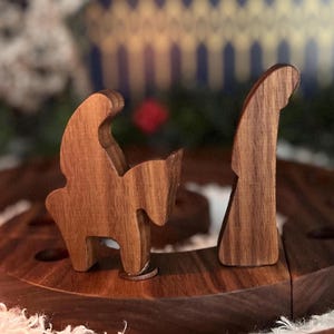 May include: Wooden nativity scene with two figures, a horse and a person, crafted from dark wood. The figures are placed on a dark wooden base, with a blurred background.