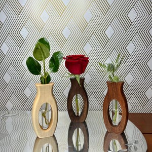 Könnte beinhalten: Drei Holz-Blumenvasen, jede mit einer einzelnen Blume oder einem Stiel. Die Vasen sind in hellem Holz, dunklem Holz und naturbelassenem Holz gehalten. Sie stehen auf einem silbernen Tablett vor einem Hintergrund mit geometrischem Muster.