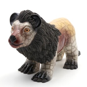 May include: A ceramic lion figurine with a black mane, white and brown body, and crackled glaze. The lion is standing on all fours and has a realistic appearance.