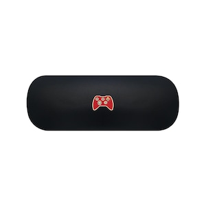May include: A matte black, oblong-shaped hard case featuring a centred graphic of a red video game controller. The controller icon displays white buttons, a directional pad, and small coloured action buttons in yellow, green, blue, and red.