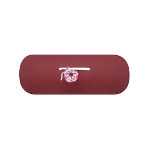 May include: A maroon, pill-shaped case featuring a centered enamel pin design. The pin depicts a silver crochet hook positioned horizontally above a circular, multi-toned pink and white crocheted yarn motif with a small hanging yarn tail.
