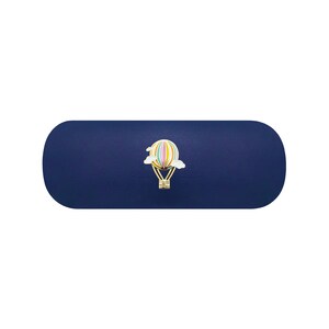May include: A dark blue, oblong, rounded-edge case featuring a centered, small, colorful hot air balloon emblem with vertical stripes in pastel tones, gold-colored basket details, and two white clouds positioned on either side of the balloon.