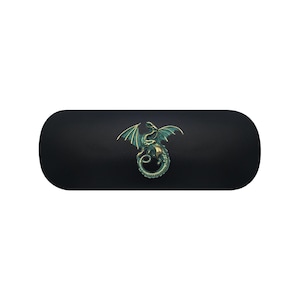 May include: A matte black, pill-shaped hard case featuring a centred, embossed metallic dragon emblem. The dragon is depicted in a weathered bronze and teal finish, with its tail curled into a circle and wings spread outward against the dark surface.