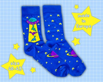 May include: A pair of blue socks with a space-themed design. The socks feature yellow stars, a UFO with dinosaurs, and planets. The socks are size 40-43.