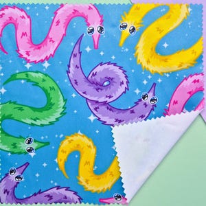 May include: A square fabric with a blue background featuring a pattern of colorful cartoon worms. The worms are in shades of pink, yellow, green, and purple, with white eyes and a starry background. The fabric is folded over, revealing a white underside.