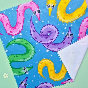May include: A square piece of fabric with a blue background featuring a repeating pattern of colorful worm-like creatures. The worms are in shades of pink, purple, yellow, and green, with white eyes and a starry sky.