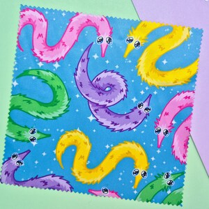 May include: A square fabric with a repeating pattern of colorful, cartoonish worm-like creatures on a blue background with white stars. The worms are in shades of pink, yellow, green, and purple, with googly eyes.
