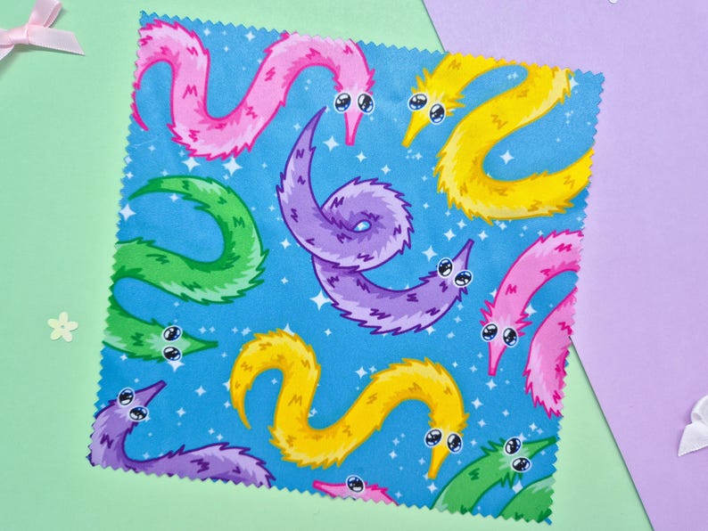 May include: A square fabric with a repeating pattern of colorful, cartoonish worm-like creatures on a blue background with white stars. The worms are in shades of pink, yellow, green, and purple, with googly eyes.