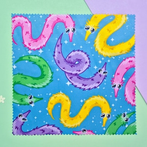May include: A square fabric with a blue background featuring a pattern of colorful, cartoonish worm-like creatures. The worms are in shades of pink, yellow, green, and purple, with white eyes and a smiling expression. The background has white star-like shapes.