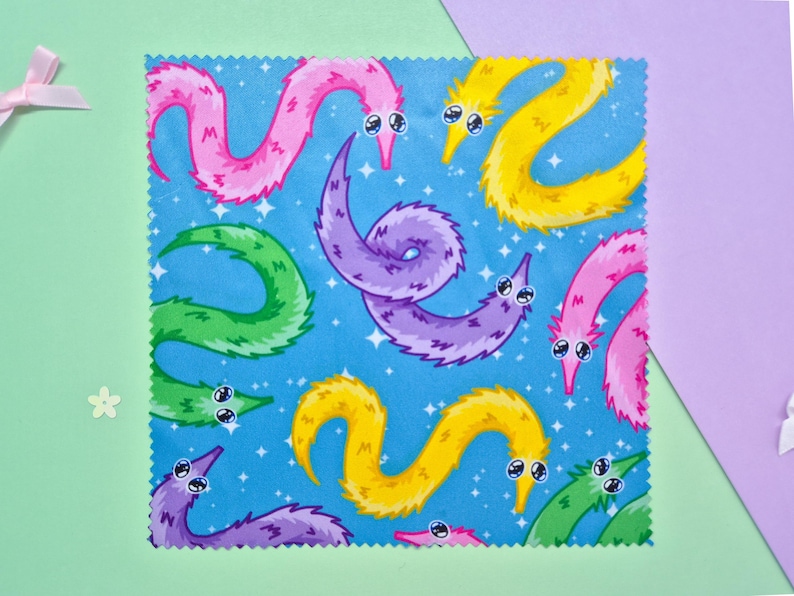 May include: A square fabric with a blue background featuring a pattern of colorful, cartoonish worm-like creatures. The worms are in shades of pink, yellow, green, and purple, with white eyes and a smiling expression. The background has white star-like shapes.