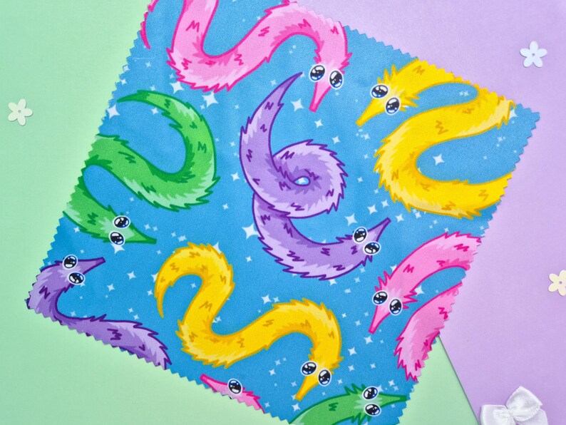 May include: A square fabric with a blue background featuring a pattern of colorful cartoon worms. The worms are in shades of pink, yellow, green, and purple, with white eyes and a starry background.
