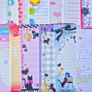 Puede incluir: Una colecci&oacute;n de art&iacute;culos de papeler&iacute;a coloridos, que incluyen blocs de notas y papeles decorativos. Los dise&ntilde;os presentan personajes de dibujos animados, notas musicales, gatos, corazones y patrones florales. La paleta de colores incluye rosa, azul, morado y amarillo.