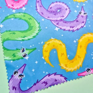 May include: A blue fabric with a repeating pattern of colorful cartoon worms with big eyes. The worms are in shades of pink, purple, yellow, and green, with a starry background.