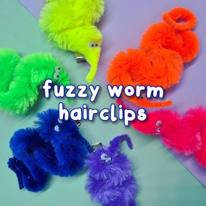 May include: A collection of colorful fuzzy worm hairclips in green, yellow, orange, pink, blue, and purple. Each clip has googly eyes and a metal clip. The text "fuzzy worm hairclips" is displayed in white.