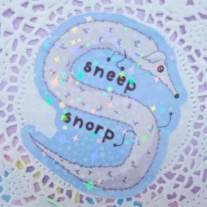 Könnte beinhalten: Ein skurriler Aufkleber mit einem wurmartigen Wesen in Weiß- und Blautönen mit holografischen Akzenten. Der Aufkleber trägt die Wörter "sneep" und "snorp" in einer verspielten Schriftart. Der Hintergrund ist hellblau mit Sternen.