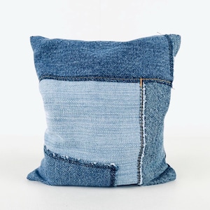 May include: A blue denim cushion with a patchwork design. The cushion is made from different shades of blue denim and has a raw edge finish.