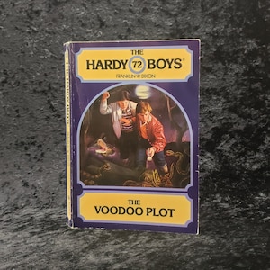 May include: The Hardy Boys #72: The Voodoo Plot book cover features a dark green and brown illustration of two boys with flashlights in a swampy area with snakes and an alligator. The book cover is blue with white and yellow text.