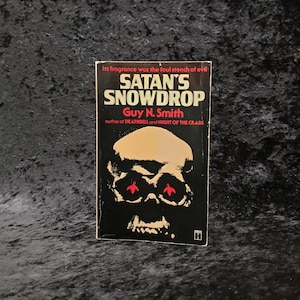 May include: A black and white book cover with a red skull illustration. The title of the book is "Satan's Snowdrop" by Guy N. Smith. The book is a horror novel.