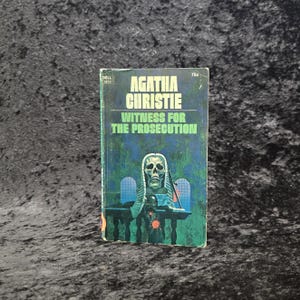 May include: Vintage paperback book titled "Witness for the Prosecution" by Agatha Christie. The cover features a skull wearing a judge's wig, set against a green and blue background. The book is a Dell edition.