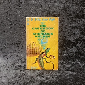 May include: A vintage paperback book titled "The Case Book of Sherlock Holmes" by Sir Arthur Conan Doyle. The cover is yellow with green and brown illustrations of a lizard, a hat, and a vase. The book is an authorized edition.