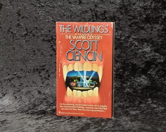 May include: A red paperback book titled "The Wildlings" by Scott Ciencin. The book cover features a close-up of a vampire's mouth with fangs, revealing a Hollywood sign in the background.