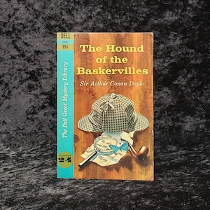 May include: Vintage paperback book cover for "The Hound of the Baskervilles" by Sir Arthur Conan Doyle. The cover features a brown and white houndstooth hat, magnifying glass, pipe, and a blue butterfly. The book is from The Dell Great Mystery Library.