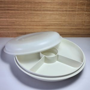 Puede incluir: Una fuente blanca de forma ovalada con tapa. La fuente está dividida en cinco secciones, con un compartimento central circular. La tapa está ligeramente entreabierta, revelando el interior. La fuente está hecha de un material plástico duradero.