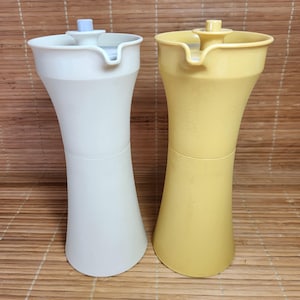 Può includere: Due bottiglie per condimenti in plastica, una bianca e una gialla, con beccucci e tappi. Le bottiglie sono progettate per contenere liquidi come olio e aceto.