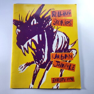 Puede incluir: Un programa de concierto vintage con fondo amarillo. La portada presenta una ilustración morada y blanca de una criatura con las palabras "Rolling Stones" y "Urban Jungle Europe 1990" en naranja y blanco.